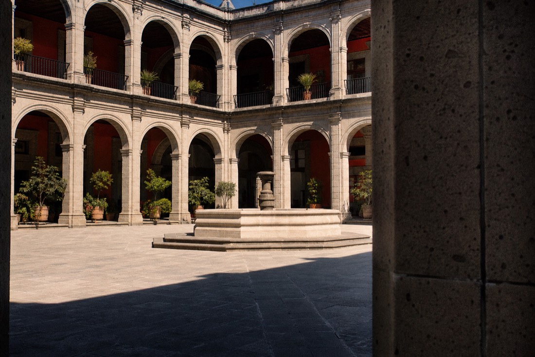 A sunlit museum courtyard with visitors crossing on a bright weekend afternoon